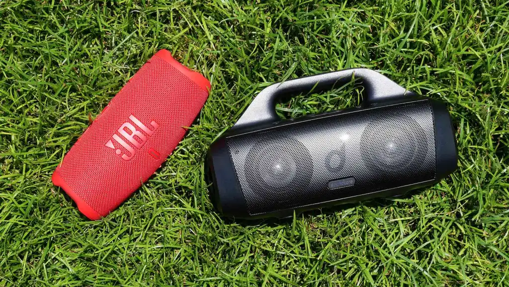image of a JBL Charge 5 VS Soundcore Motion Boom laying in the grass